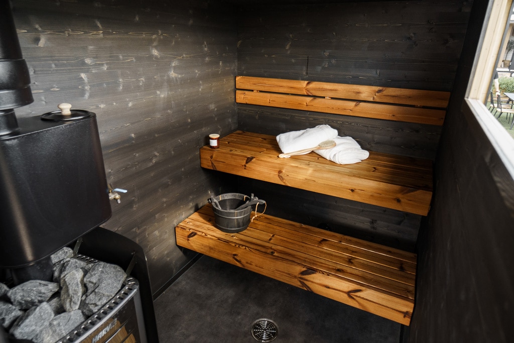 Lapelland Saunawelt: Holzbänke, Eimer mit Schöpfkelle, Handtücher, Saunaofen mit Steinen in einer Holzsauna.