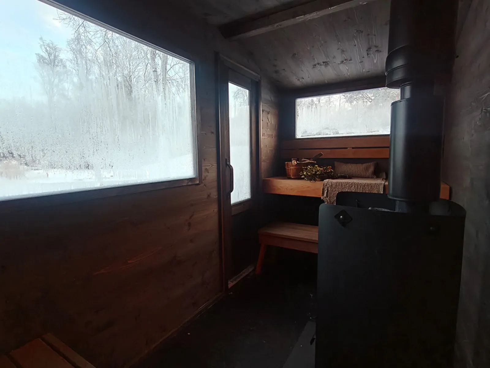Lapelland Saunawelt: Kleine Holzsauna mit mattierten Fenstern, einer Bank, Handtüchern, einem Korb und einem schwarzen Ofen vorne.