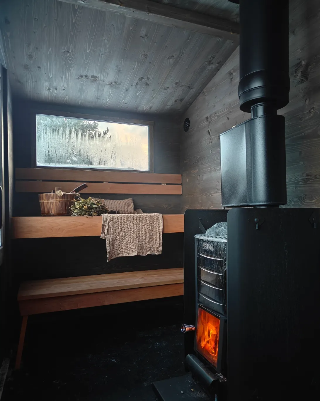 Lapelland Saunawelt: Holzgetäfelte Sauna mit 2 Bänken, Holzofen, verglasten Fenstern, Handtüchern und Birkenzweigen.