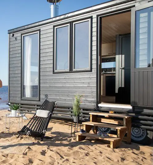 Das schwarze Tiny House auf Rädern bei Lapelland Saunawelt am Wasser, mit Stufen, Liege und Pflanzen.