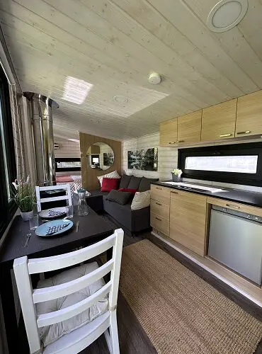Modernes Tiny House mit Holzvertäfelung, kleiner Küche, Esstisch, Sofa und viel Licht, inspiriert von der Saunawelt in Lappland.