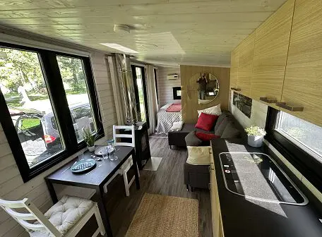 Gemütliches Tiny House in der Lapelland-Saunawelt: Kochnische, Esstisch, Sofa, Bett und helle Fenster.