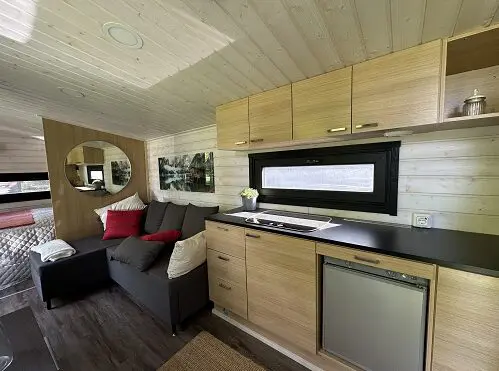 Lapelland Saunawelt: Kleine, moderne Küche mit Holzschränken, Sofa, Spiegel und Minikühlschrank im Tiny House.