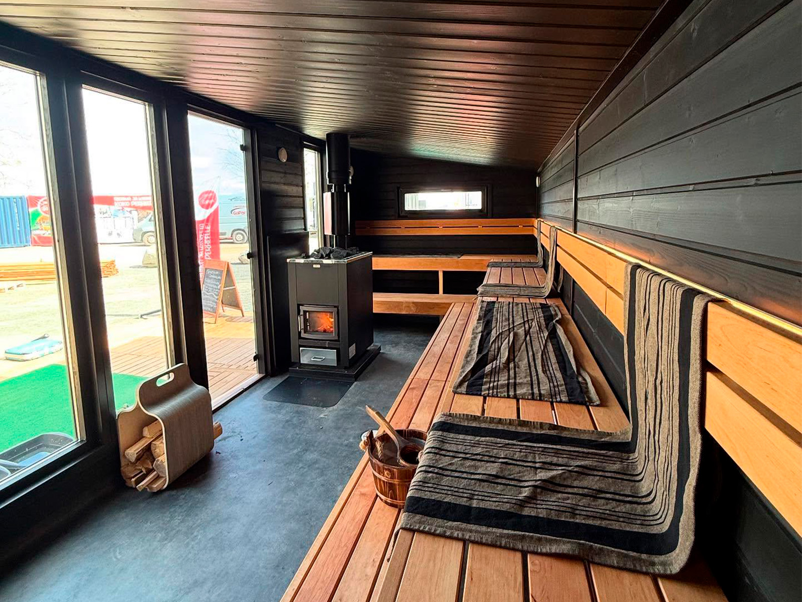 Lapelland Saunawelt: Moderne Sauna mit Holzbänken, gestreiften Handtüchern, Ofen und großen Fenstern.