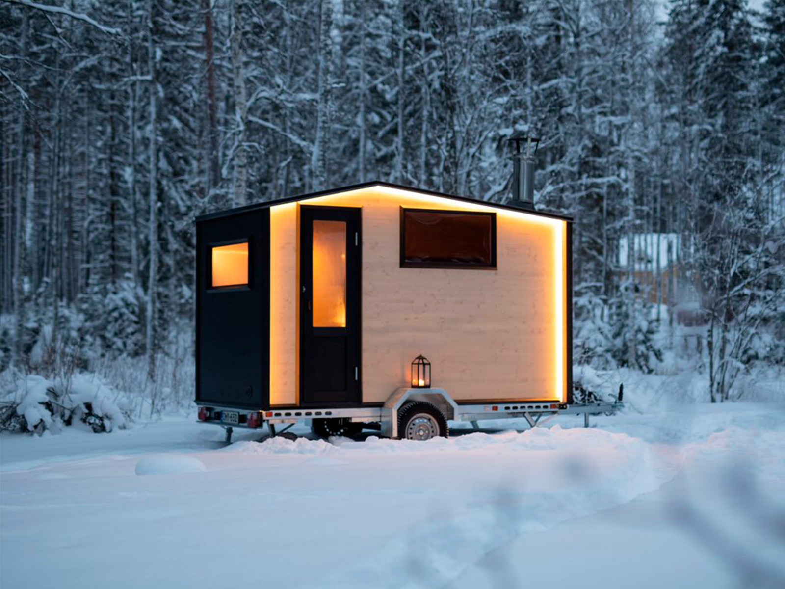 Lapelland Saunawelt: Ein modernes Tiny House mit leuchtenden Kanten steht auf einem Anhänger im verschneiten Wald.